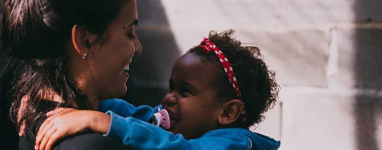 A woman picks up a small child, both are smiling at each other