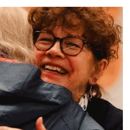 Woman smiles as she hugs another for emotional support.
